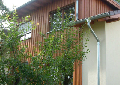 Mehrgenerationenhaus als Anbau mit hellbraun lasierter Boden-Deckel-Schalung aus Lärche